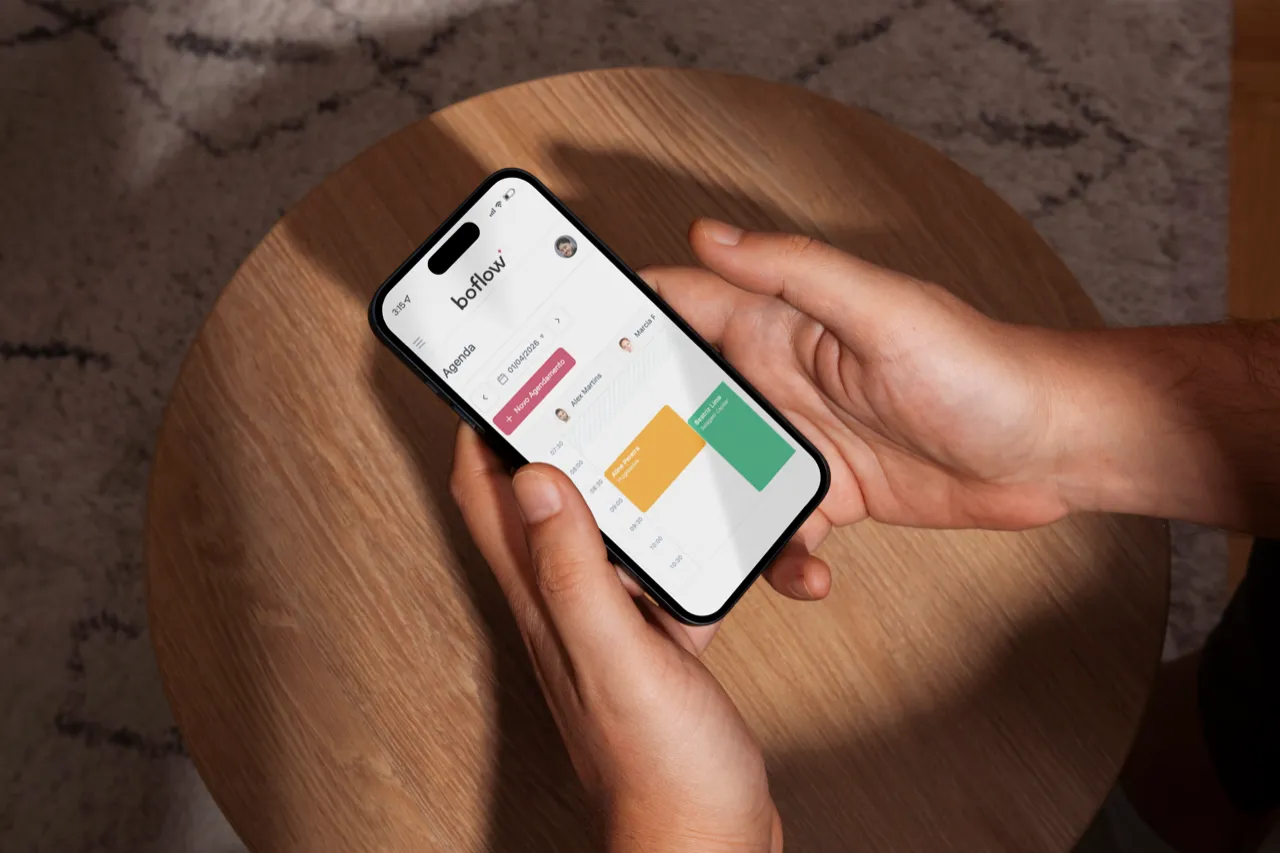 App Boflow no celular — mão segurando smartphone sobre laptop
